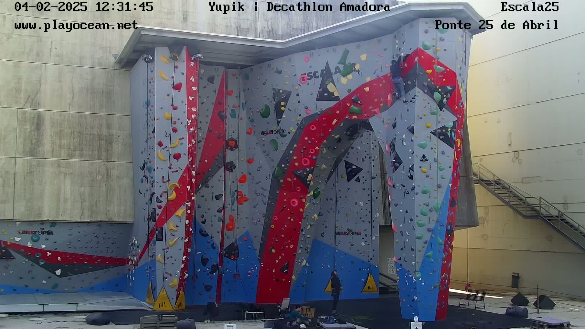 A large, brightly colored outdoor climbing wall with several people near the base.