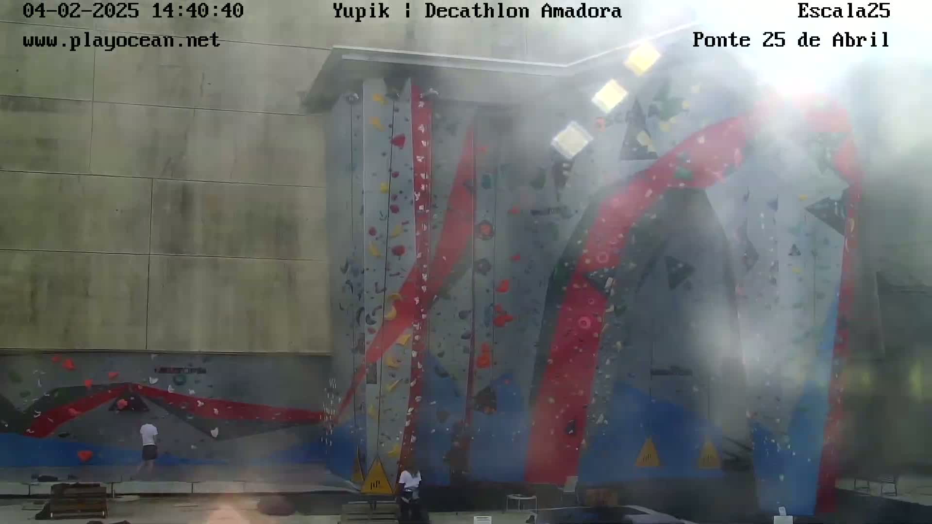 A large outdoor climbing wall with several people climbing and a hazy atmosphere.