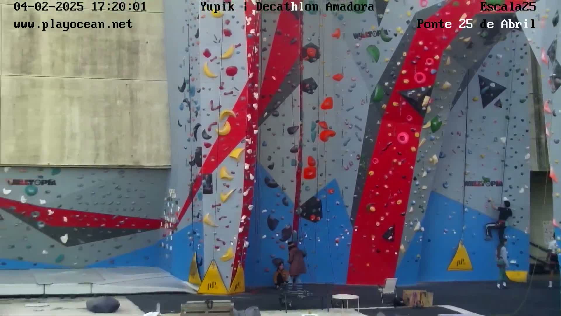 A large, colorful indoor climbing wall with several people climbing and observing.