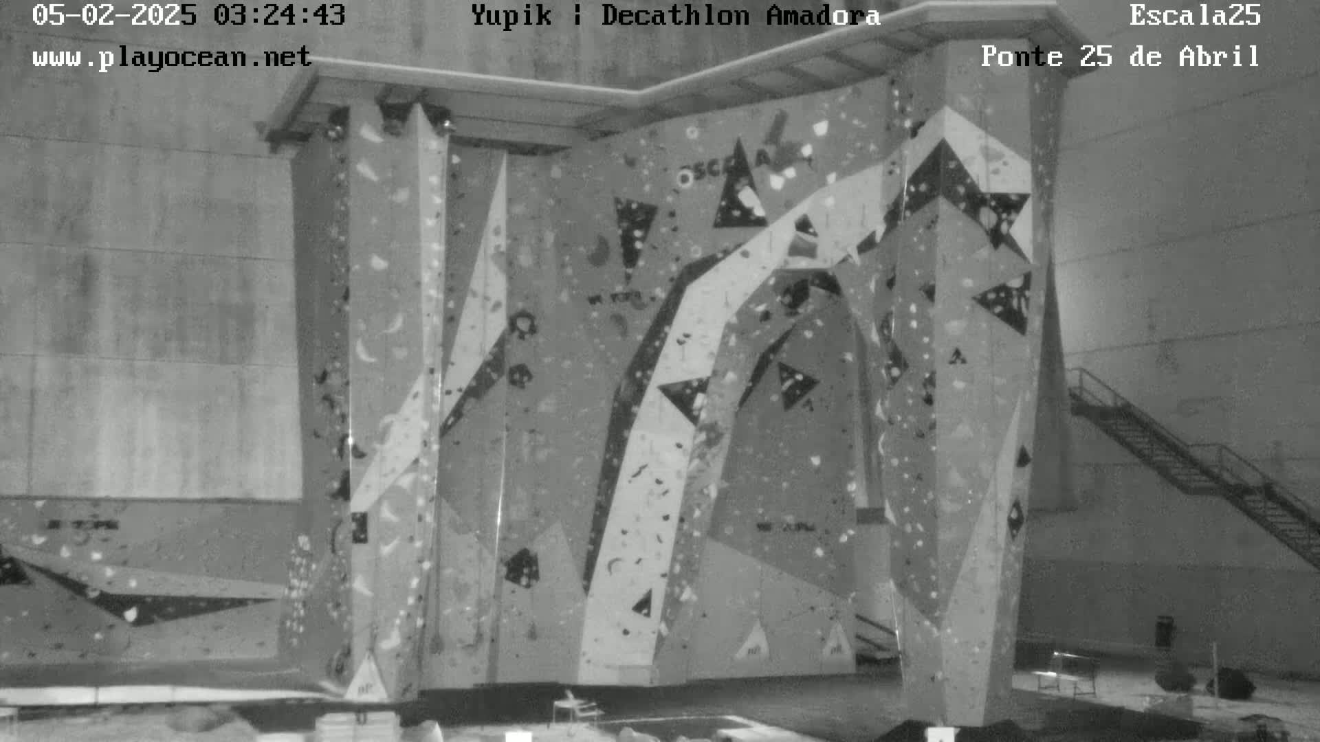 A grayscale image shows an indoor climbing wall with various holds affixed to its surface.