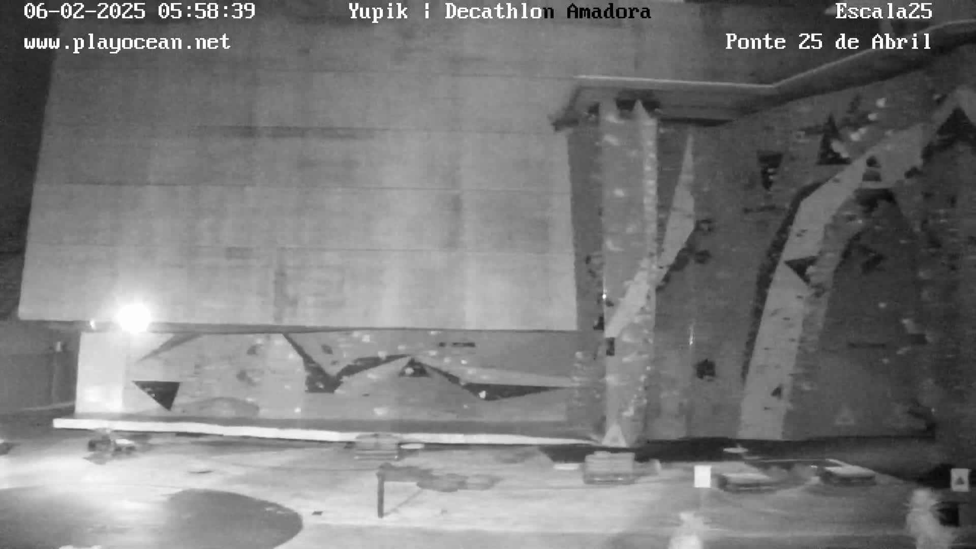 A nighttime, outdoor view of a large, flat, gray wall with an attached climbing wall.