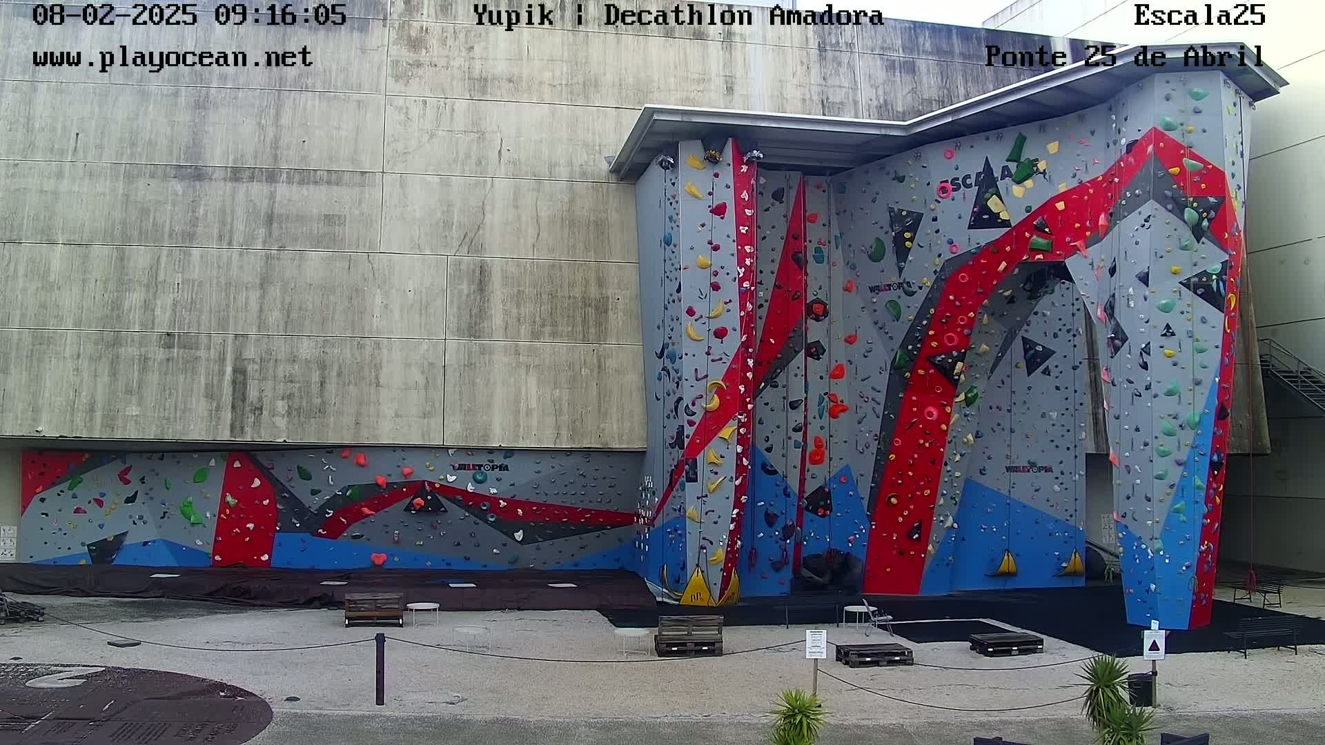 An outdoor view of a large, multi-colored climbing wall attached to a building on an overcast day.