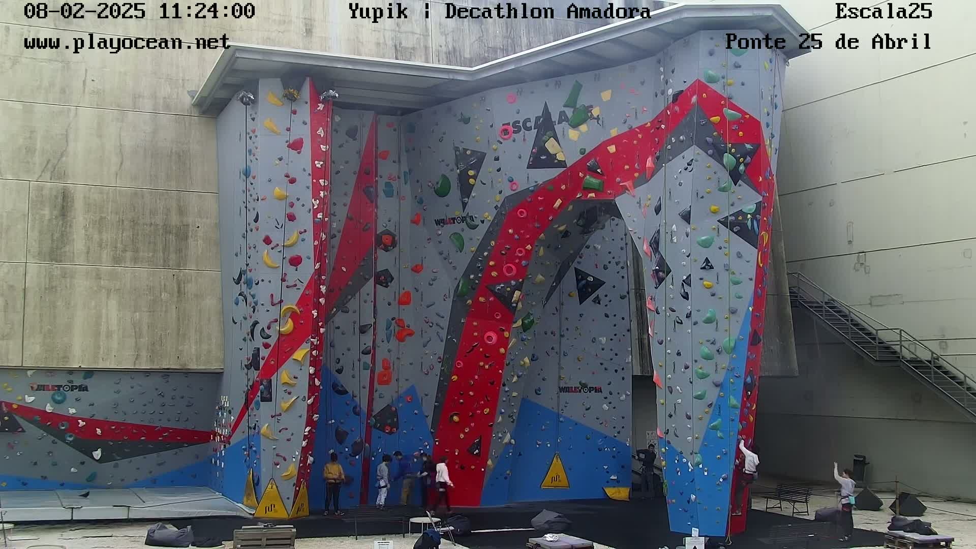 A large indoor climbing wall with various colored holds and several people at its base.