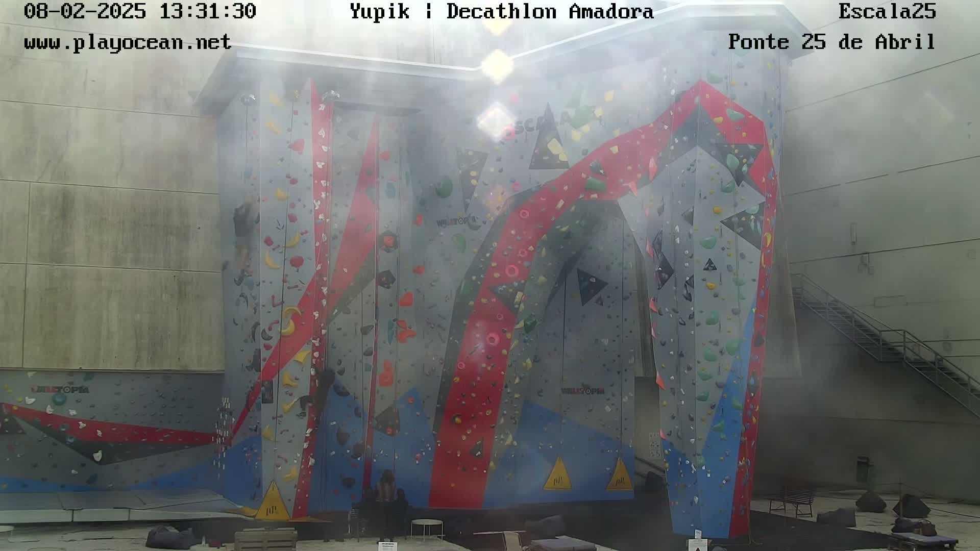 A large, colorful indoor climbing wall is visible, with a hazy atmosphere present.