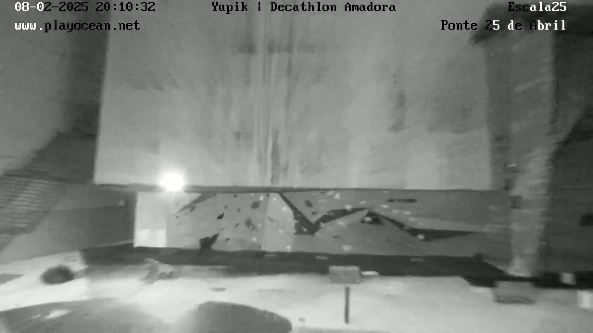A nighttime, grayscale image shows a low-angle view of a climbing wall with various holds and a brightly lit area at the bottom.