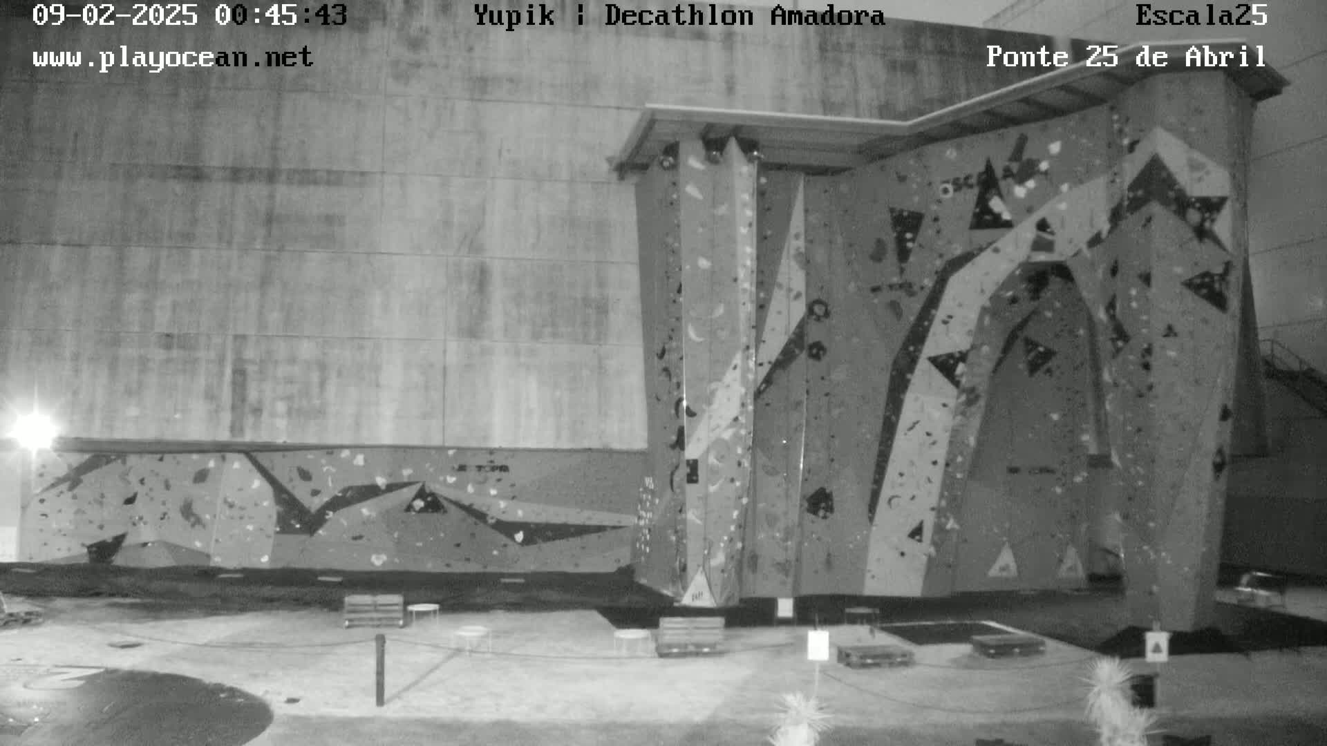 A nighttime, black-and-white image shows an outdoor climbing wall affixed to a large building.
