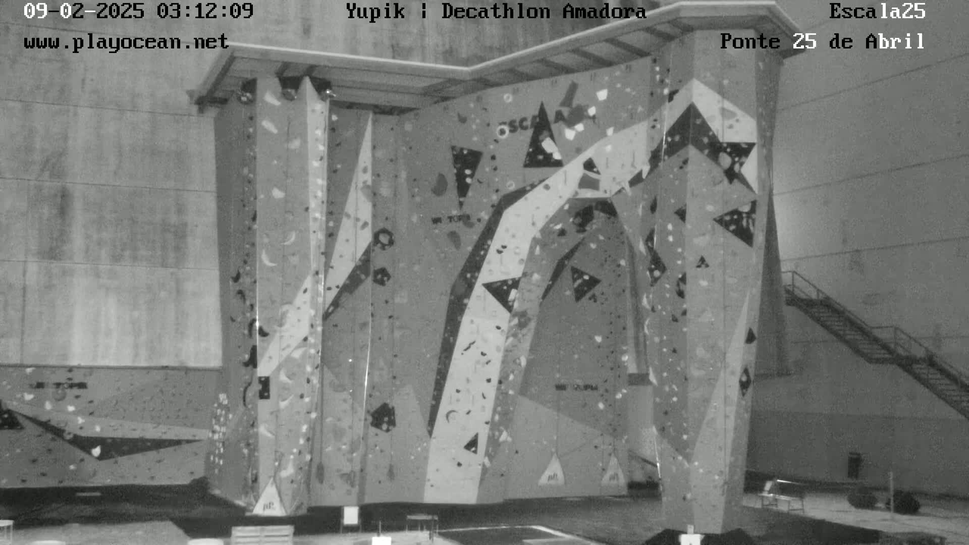 A large indoor climbing wall with various holds and patterns is shown in a grayscale image.