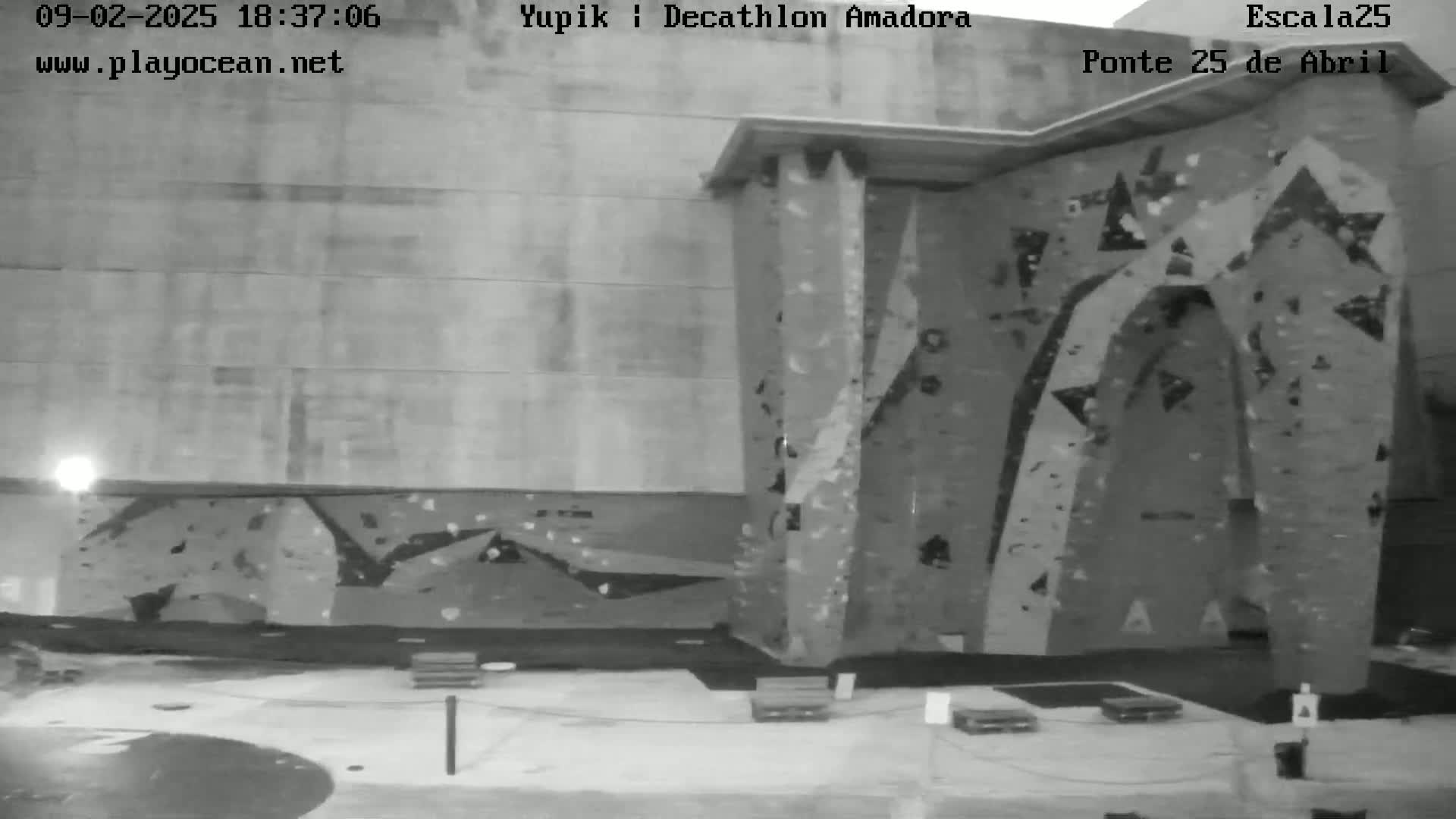 A nighttime grayscale image shows an outdoor climbing wall attached to a building.