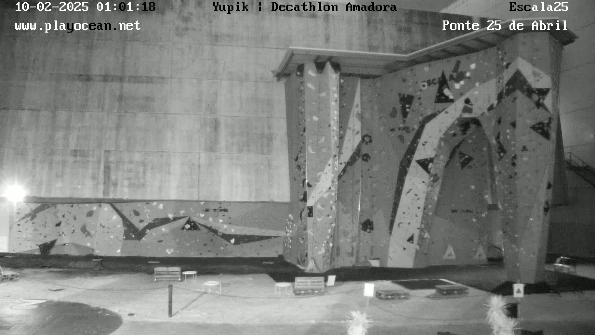 A grayscale nighttime image shows an indoor climbing wall with various holds and features.