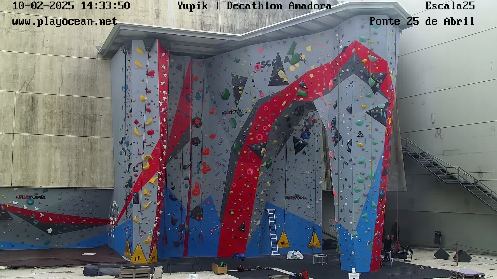 A large, colorful indoor climbing wall with various holds and routes, situated in a building.