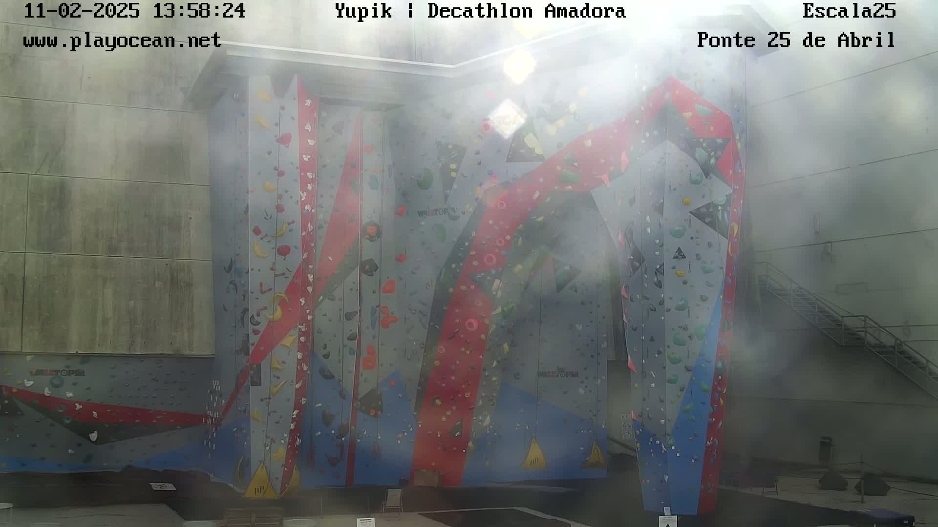 A large, brightly colored indoor climbing wall is visible through a hazy atmosphere.