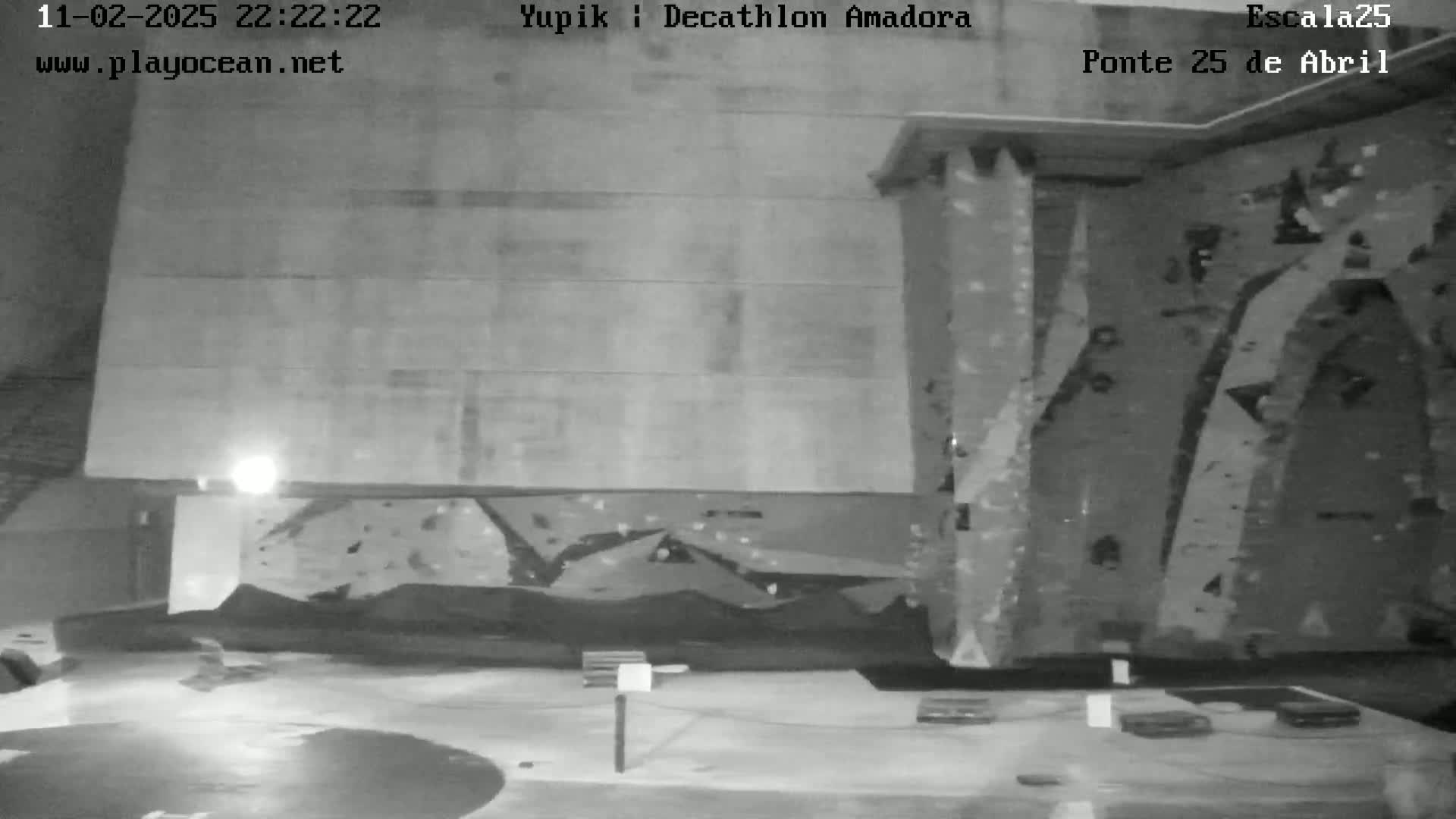 A nighttime, indoor view of a climbing wall with a smooth concrete floor.