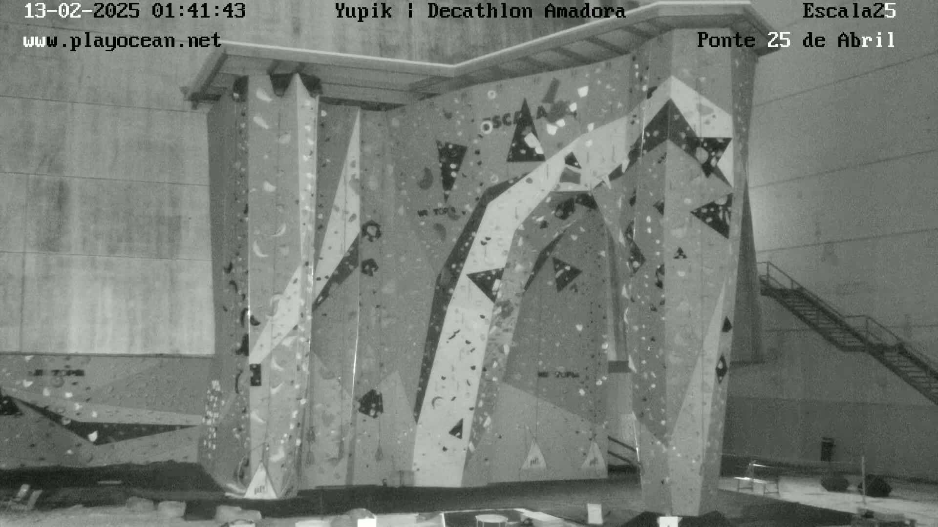 A grayscale image shows an indoor climbing wall with various holds and patterns against a concrete wall.