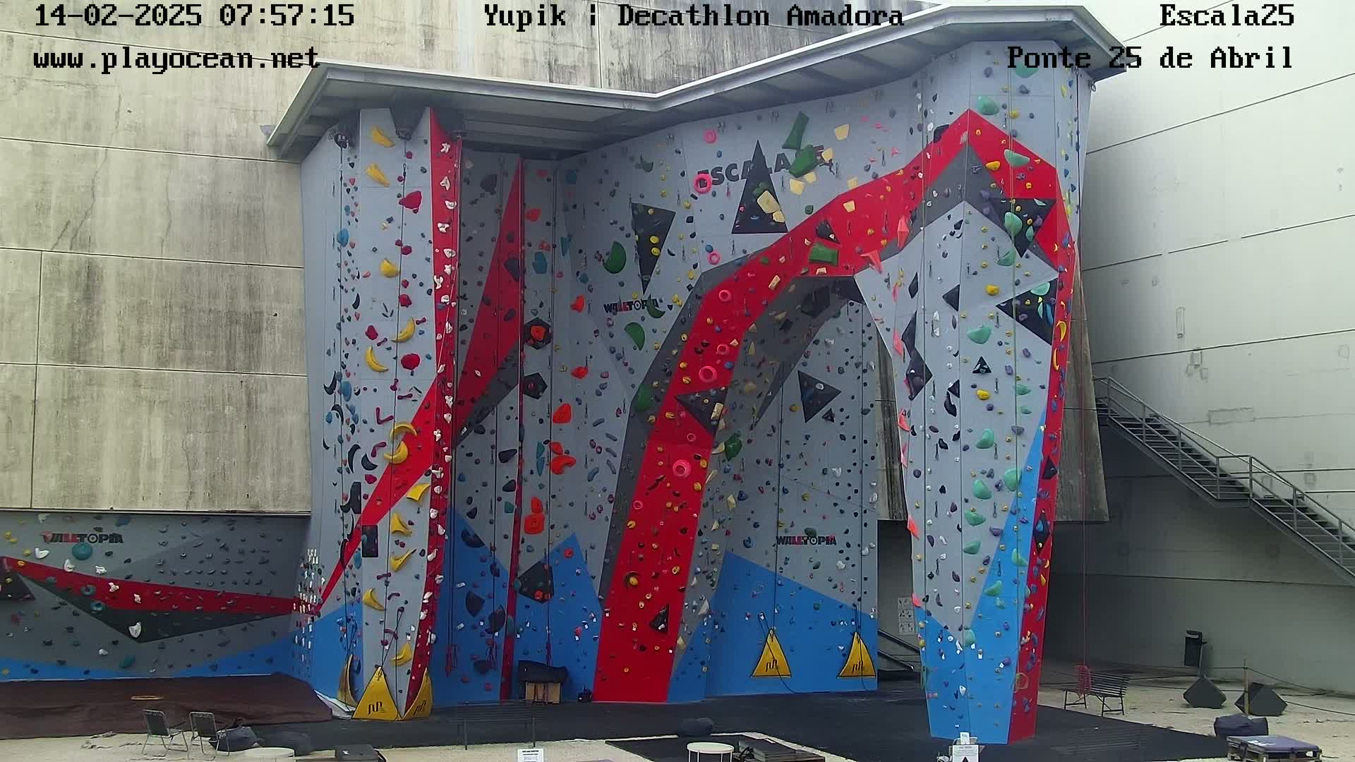 A large, multi-colored indoor climbing wall stands against a gray building on an overcast day.