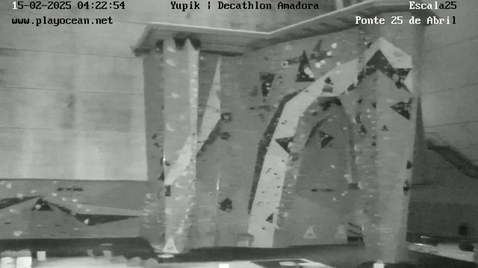 A grayscale image shows an indoor climbing wall with various holds and textures.