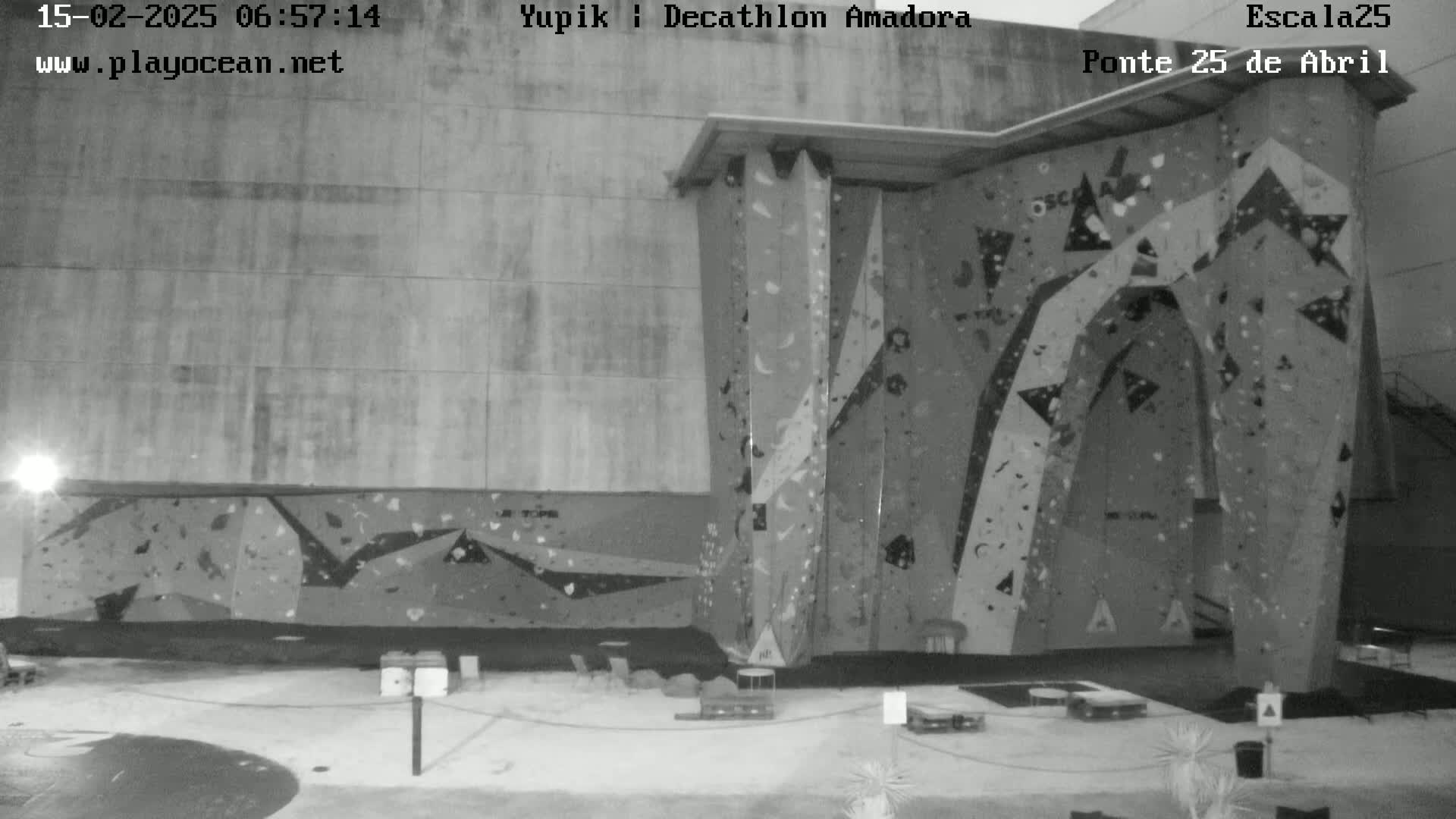 A grayscale image shows an outdoor, overcast scene of a large climbing wall against a building.