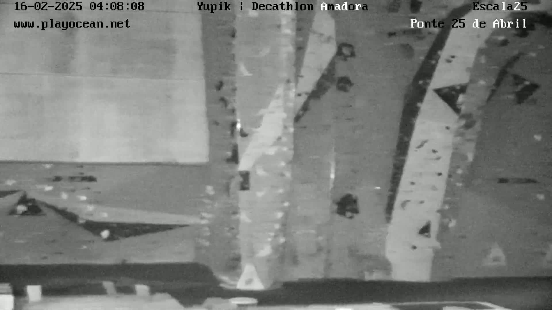 A grainy, low-light black and white image shows a textured wall with vertical streaks and a dark, possibly paved area at the bottom.