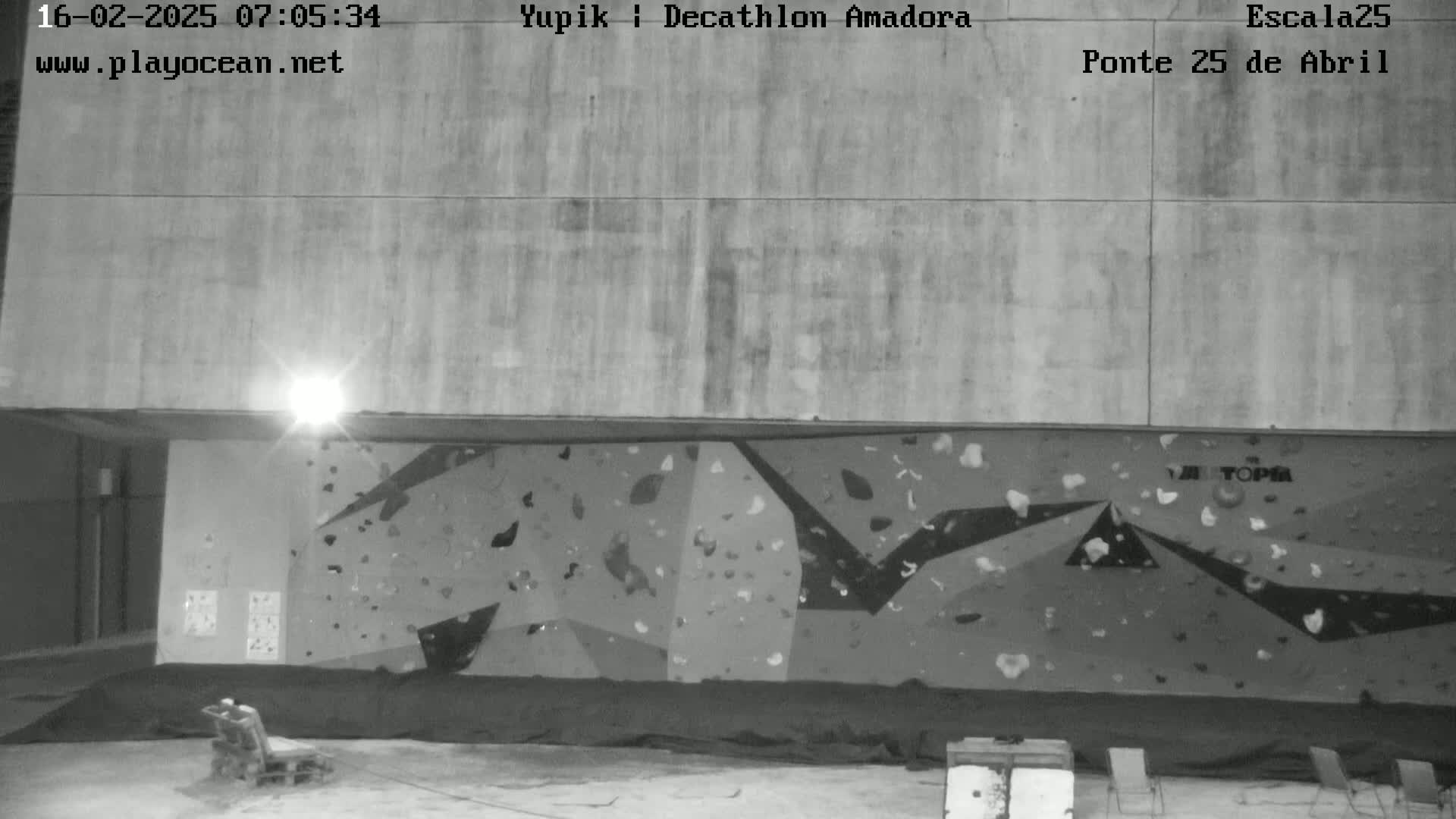 A black and white nighttime image shows an indoor climbing wall beneath a large concrete overhang.