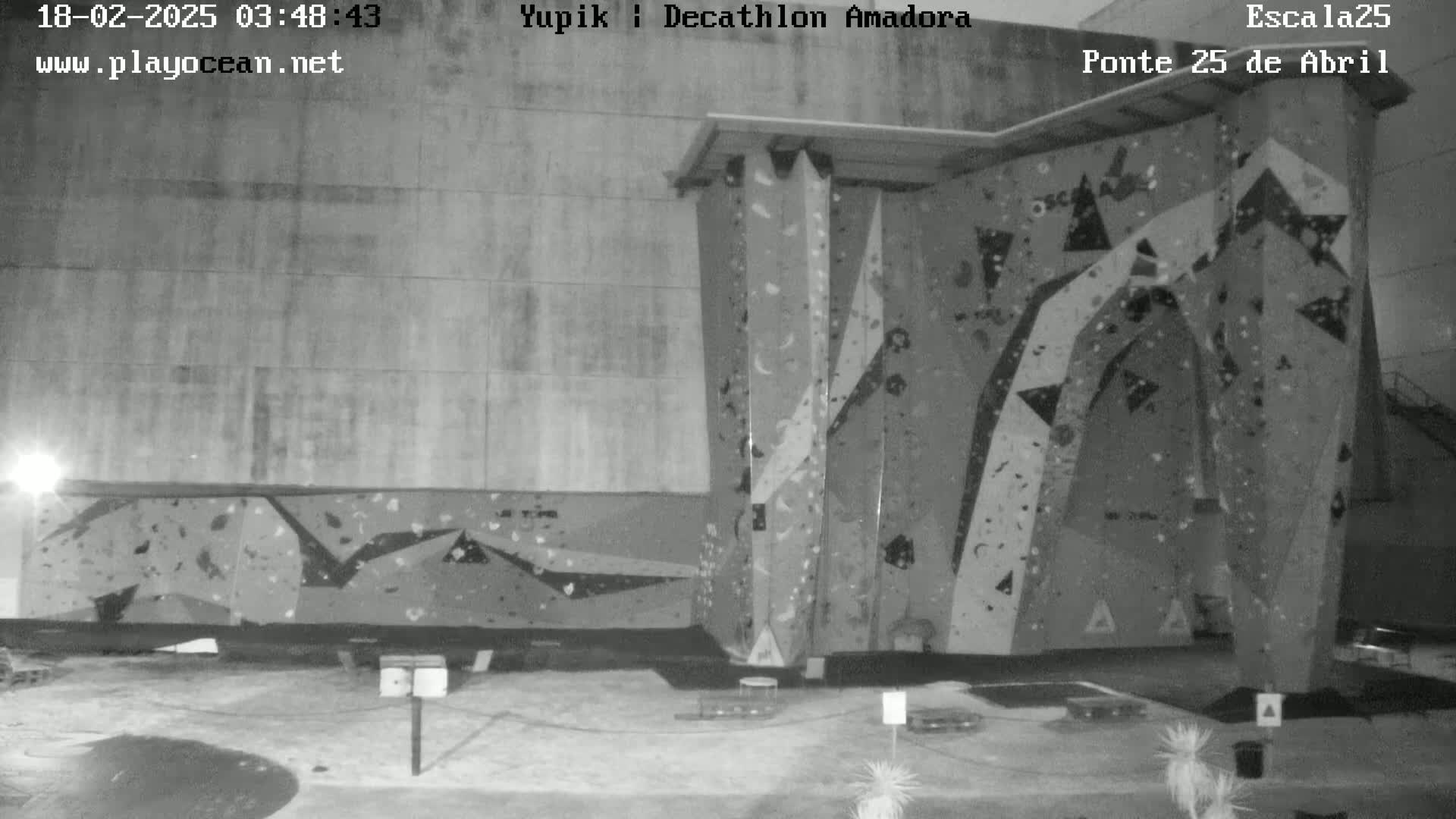 A nighttime, black-and-white view of an outdoor climbing wall attached to a building.