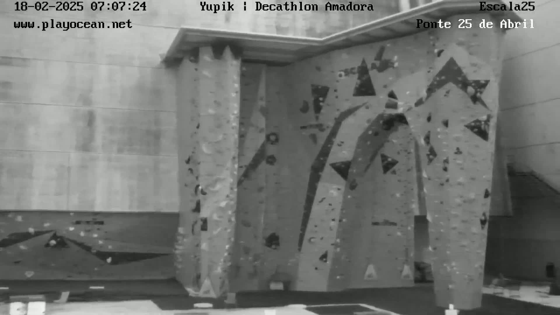 A grayscale image shows an indoor climbing wall with various holds and textures.