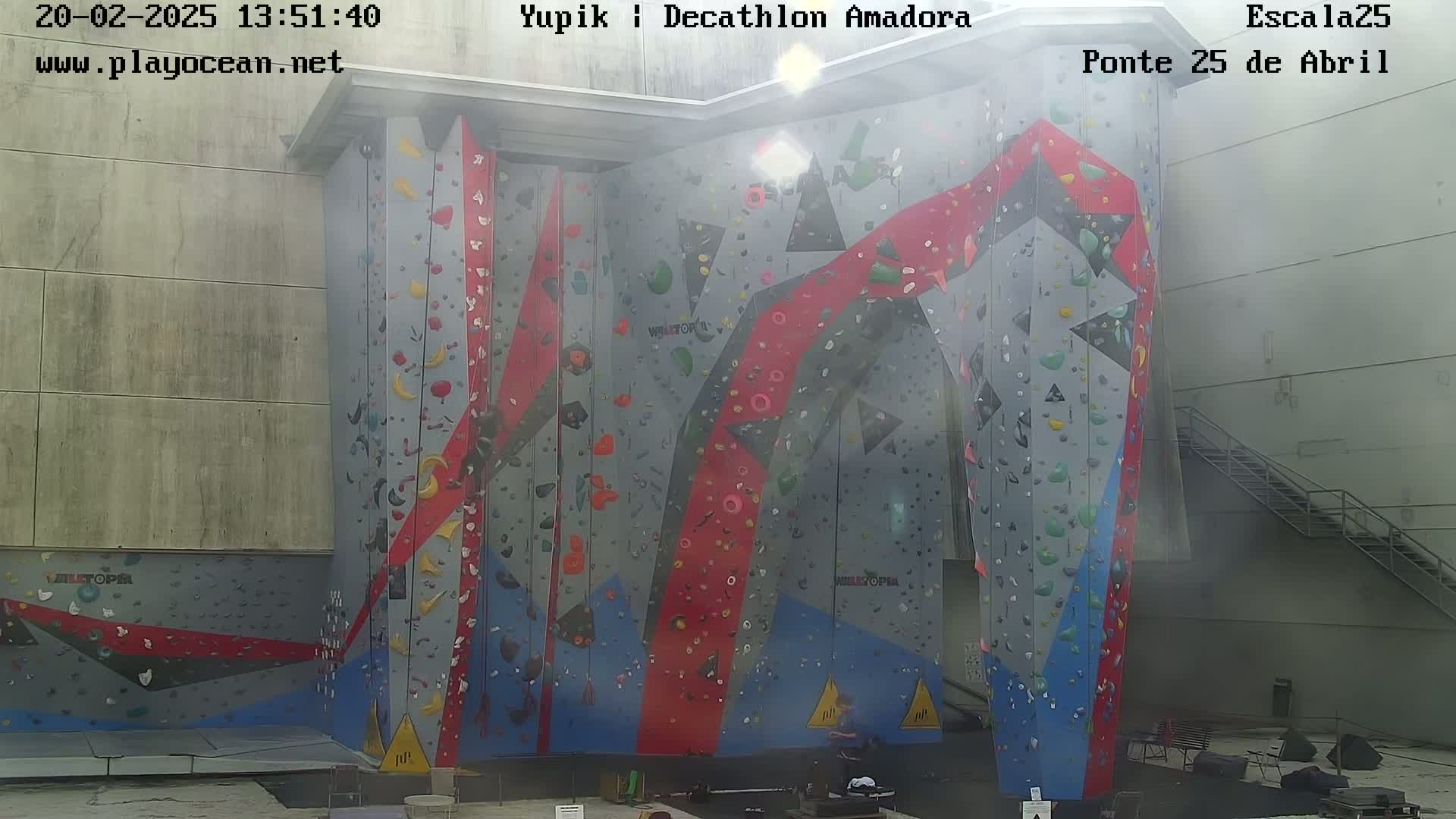 A large, colorful indoor climbing wall is partially visible under hazy sunlight.