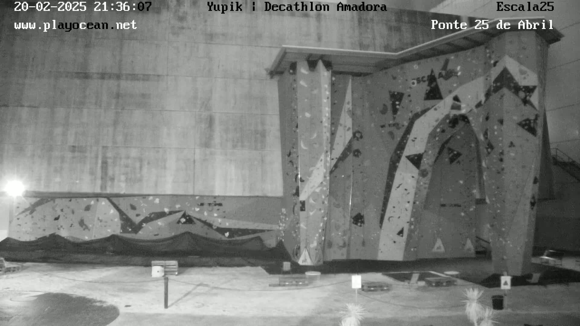 A black-and-white nighttime image shows an indoor climbing wall with various holds and features.