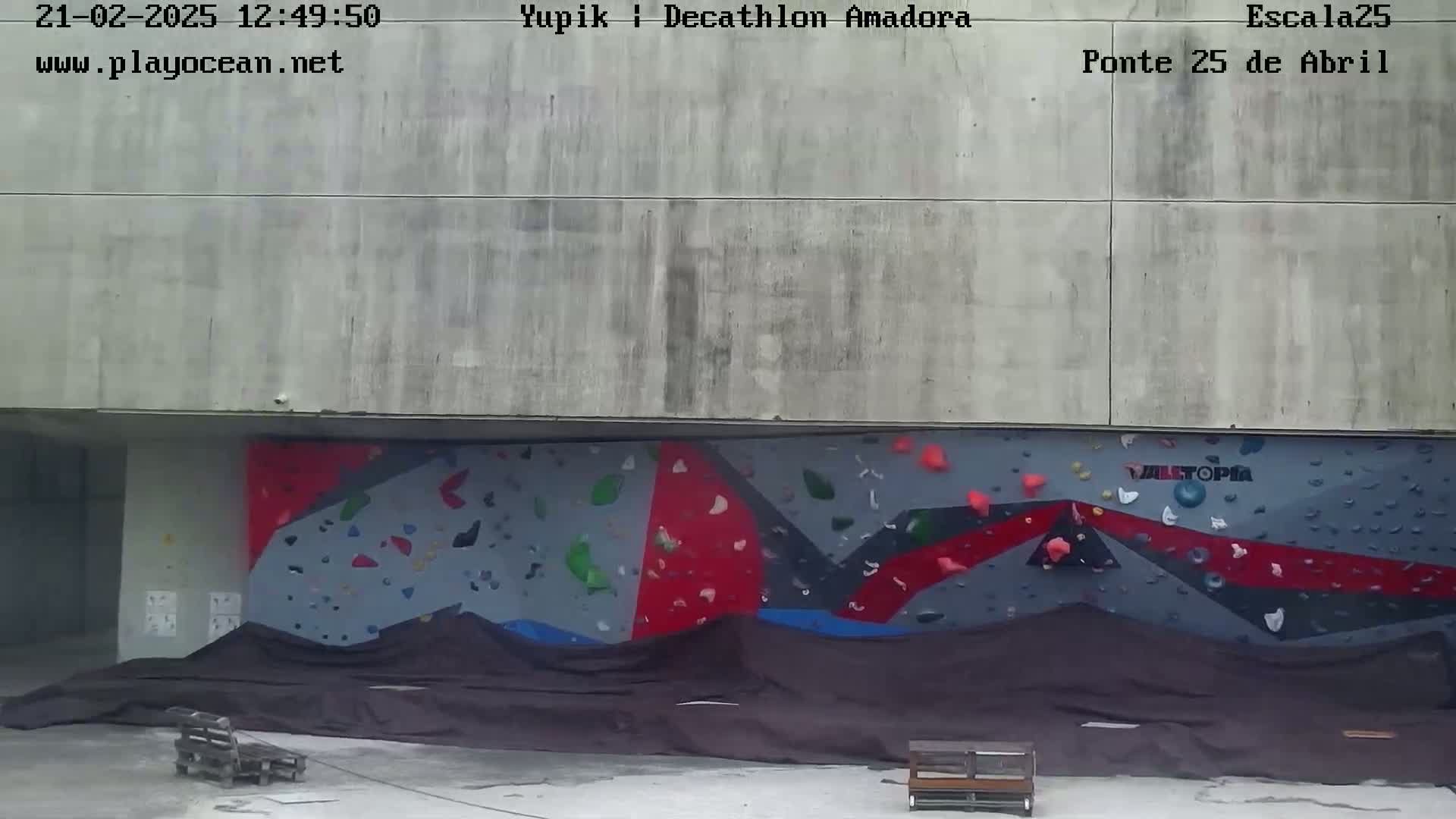 A large, partially covered outdoor climbing wall is situated beneath a concrete structure.