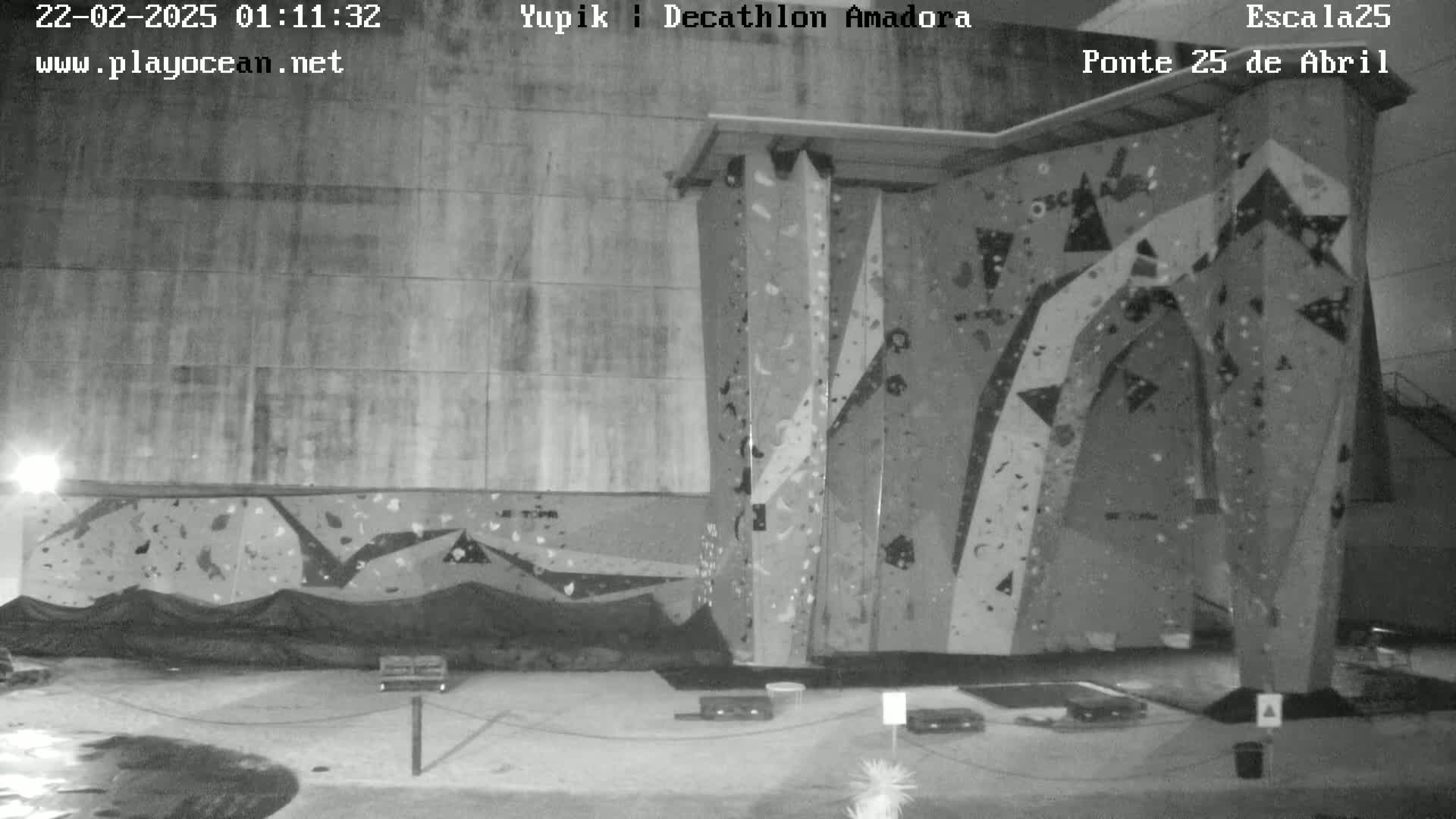 A nighttime, black and white image shows an indoor rock climbing wall.