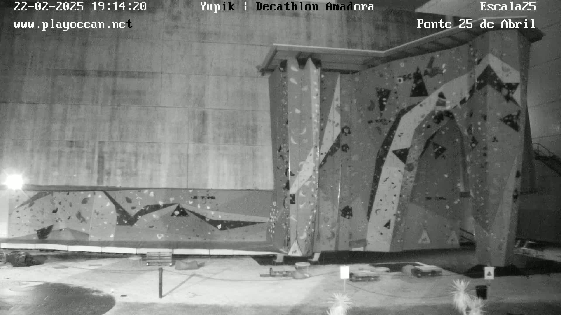 A nighttime black and white image shows two large climbing walls outdoors.
