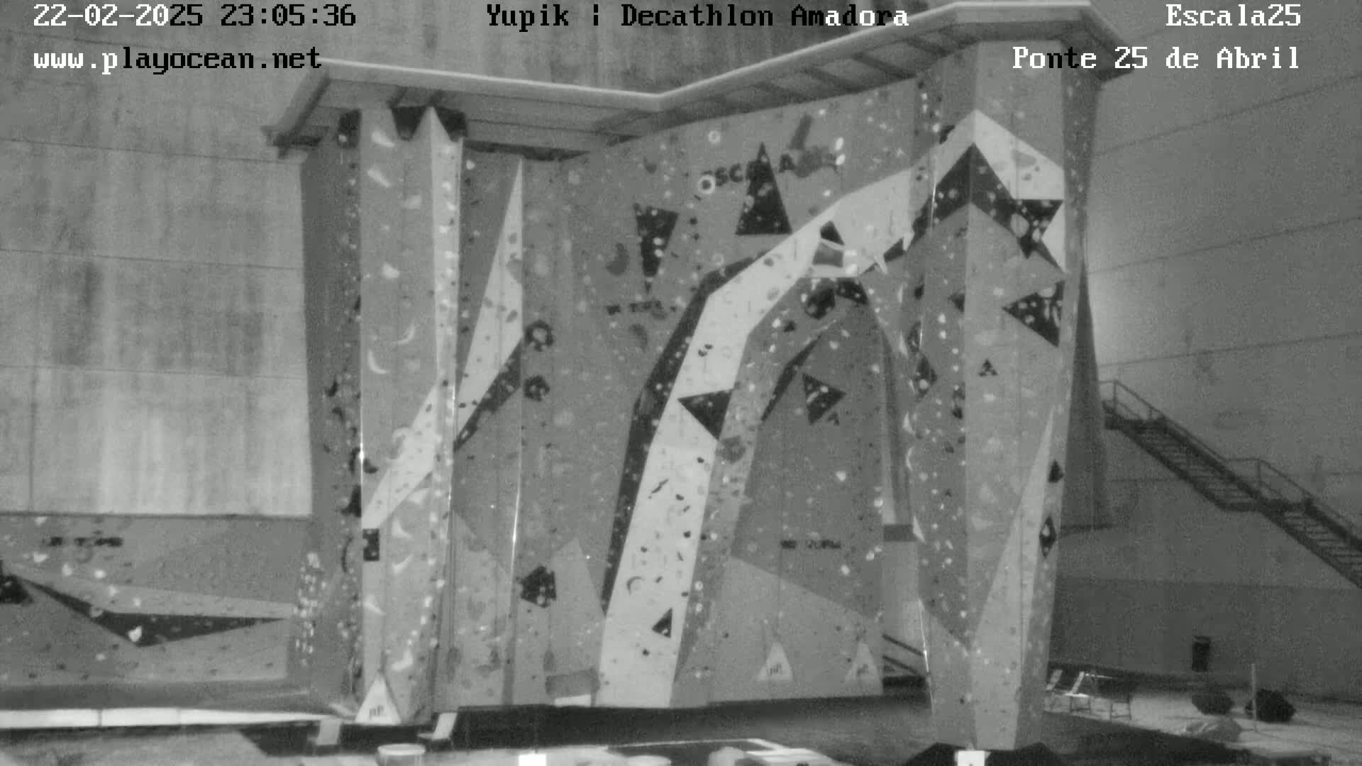 A large indoor climbing wall with various colored holds stands in a dimly lit room.