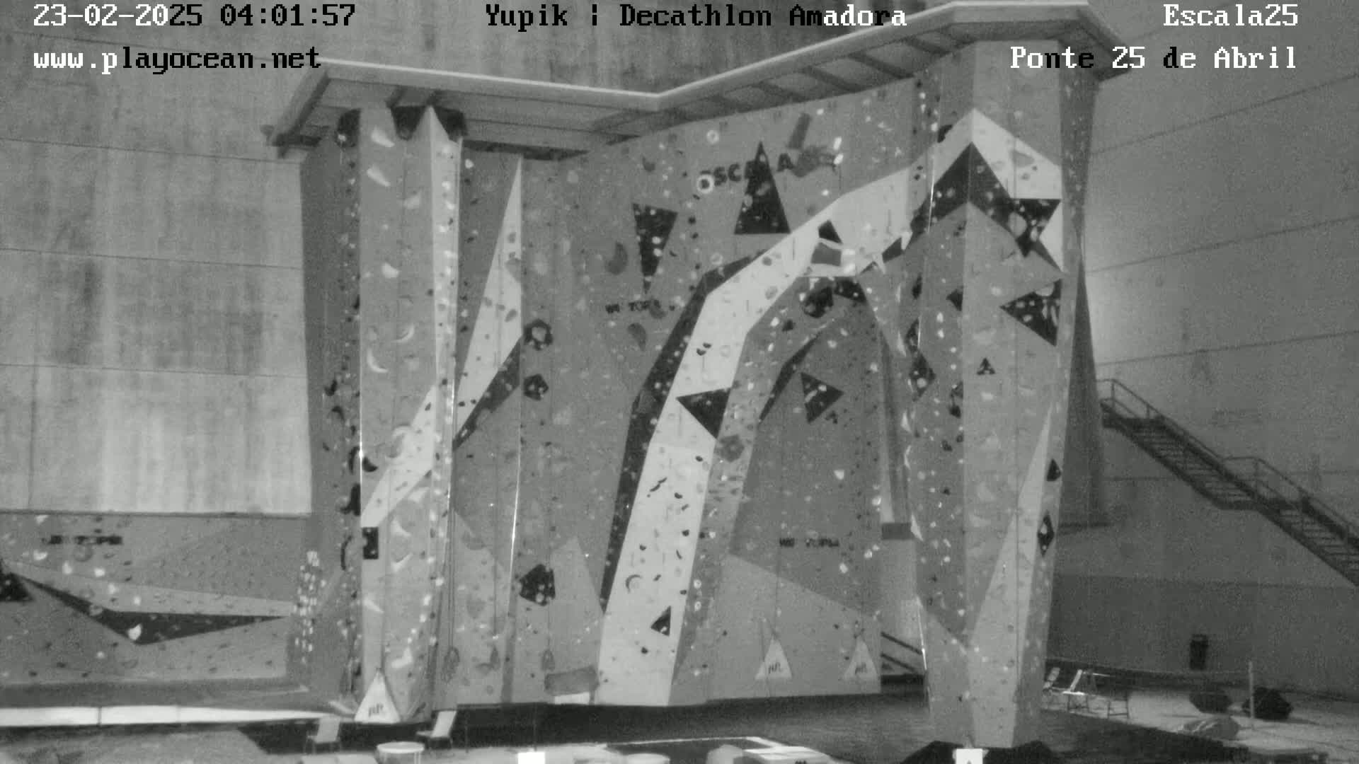 A grayscale image shows an indoor climbing wall with various holds and geometric shapes.