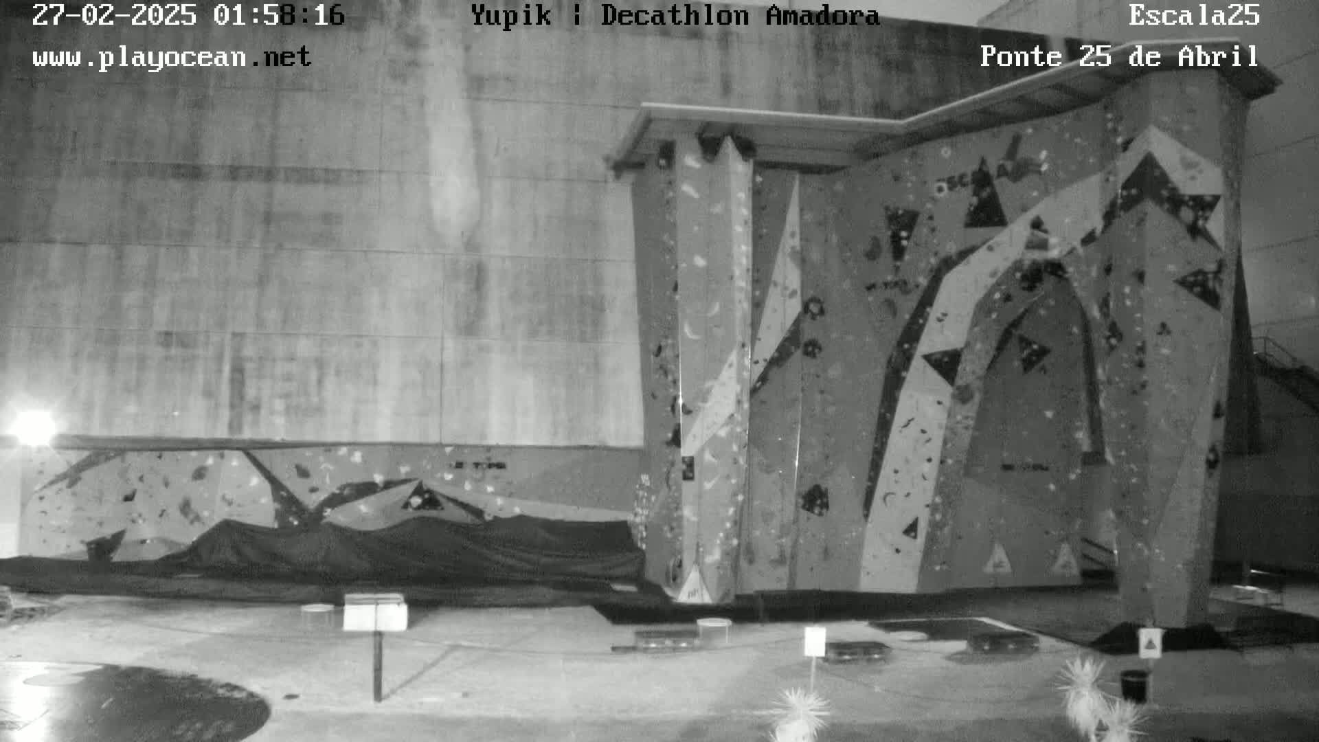 A nighttime grayscale image shows an outdoor climbing wall under a dark sky.