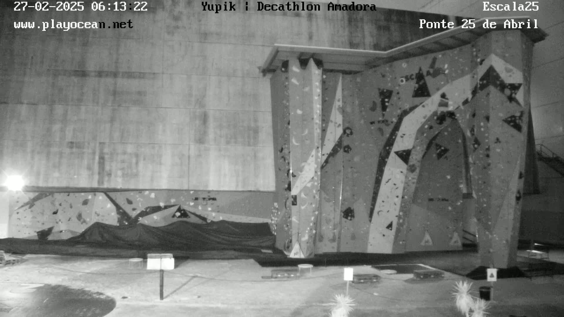 A black-and-white nighttime image shows an indoor climbing wall with various holds and a tarp covering the base.