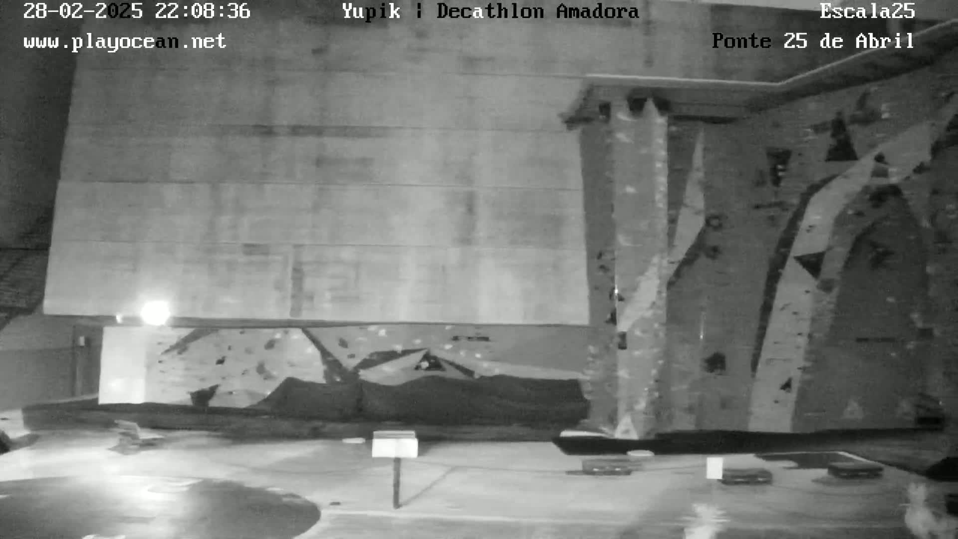 A grayscale nighttime image shows an indoor rock climbing wall in a dimly lit area.