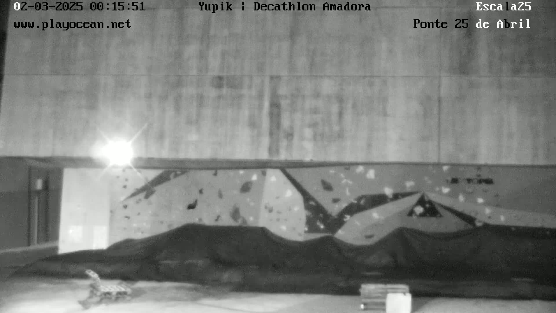 A grayscale image shows an indoor climbing wall covered with a dark tarp, with a bright light source visible in the upper left corner.