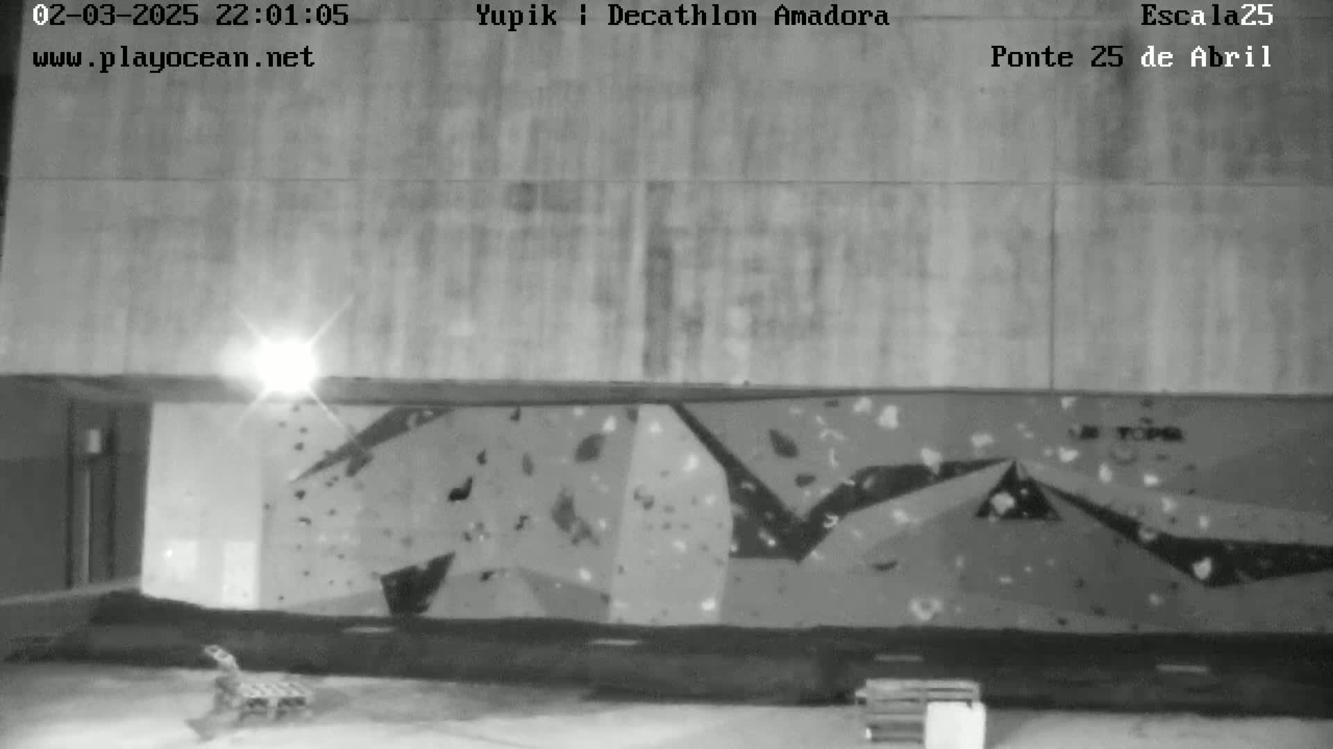 A nighttime, black-and-white view of an outdoor climbing wall under a light source.