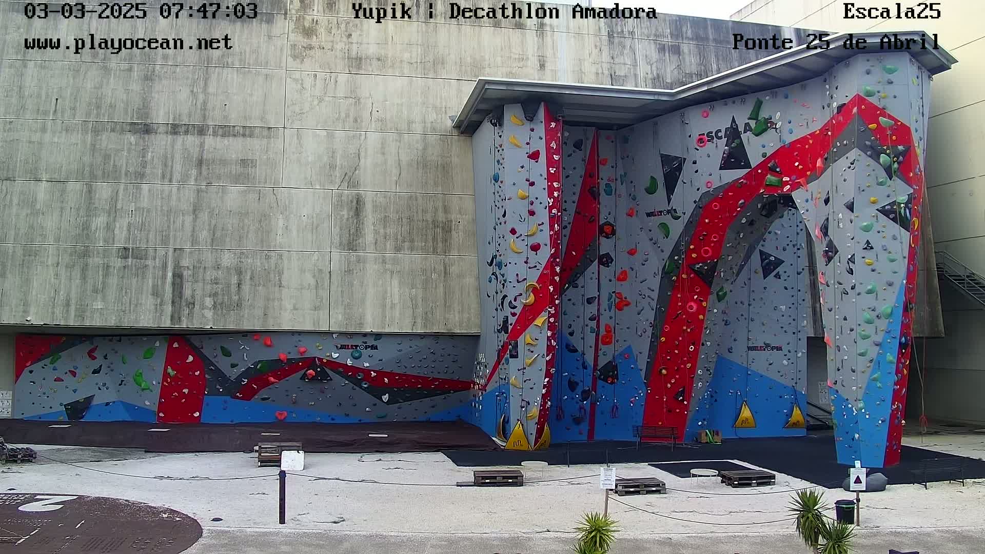 An outdoor, daytime view of a large, multicolored climbing wall affixed to a building.