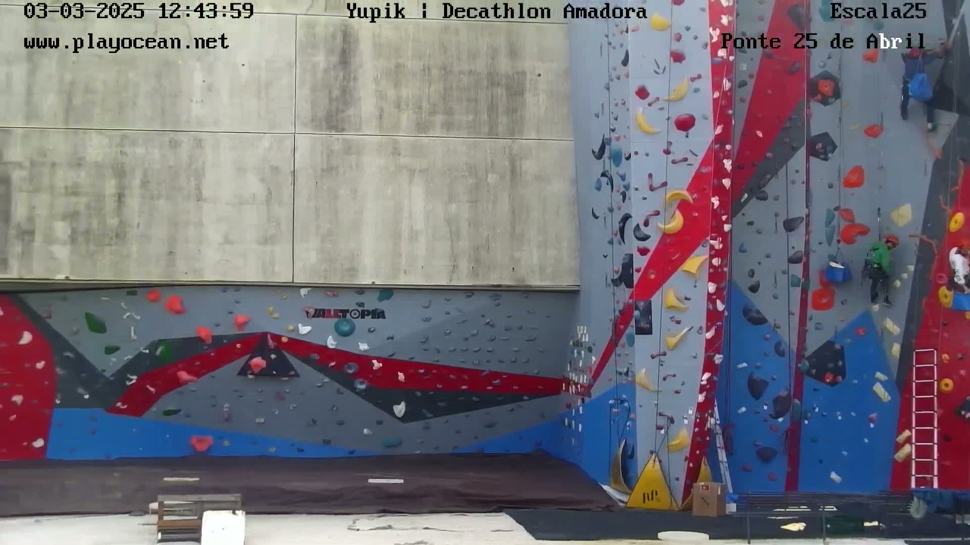 An outdoor climbing wall with various colored holds and several people climbing.