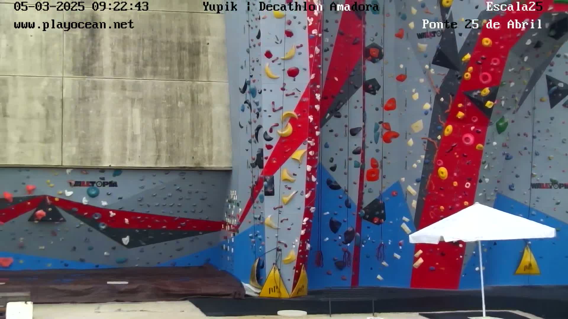 A large, colorful indoor climbing wall is visible, with a white patio umbrella in the foreground.