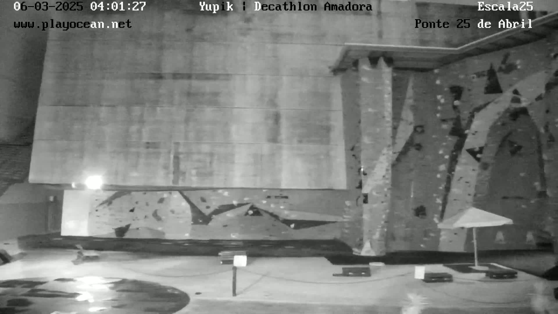 A black and white night-time image shows an indoor rock climbing wall with a wet floor.