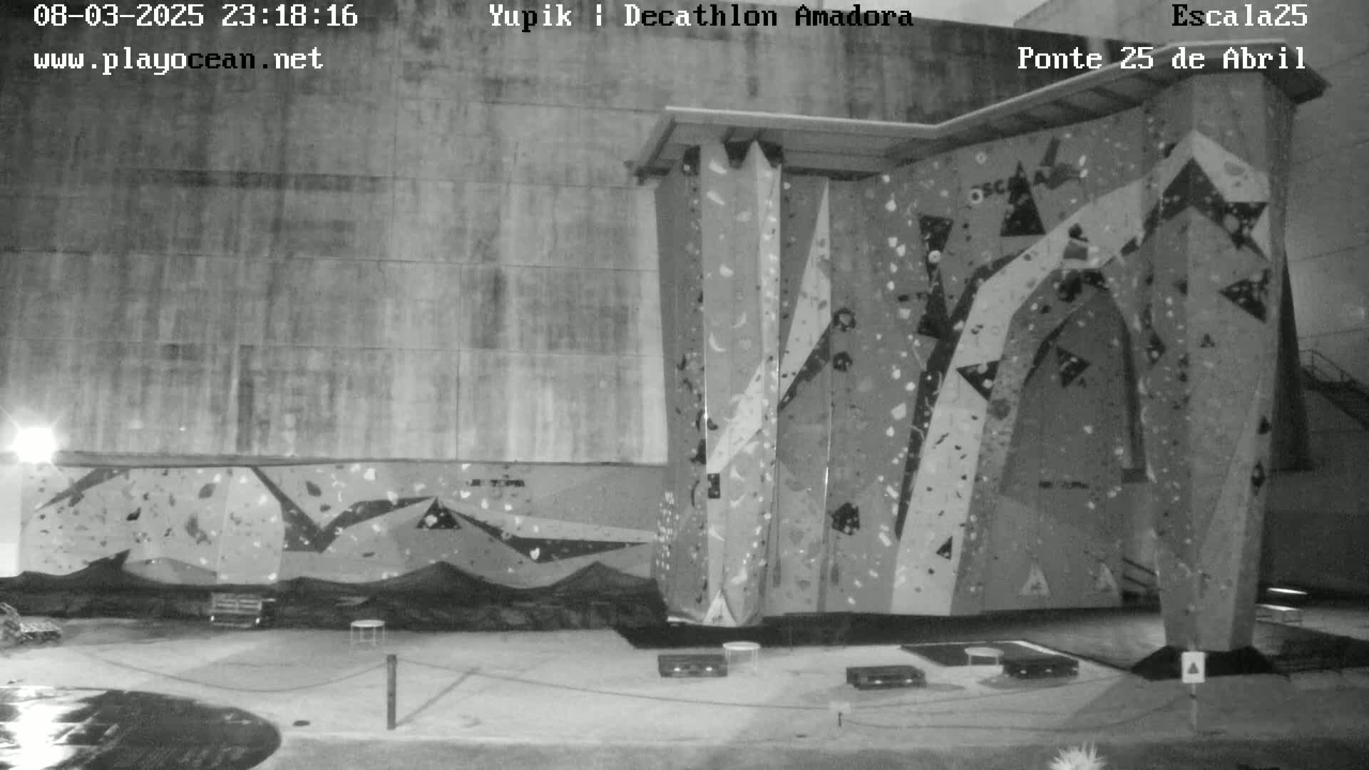 A nighttime, black-and-white view of an outdoor climbing wall situated against a large building.