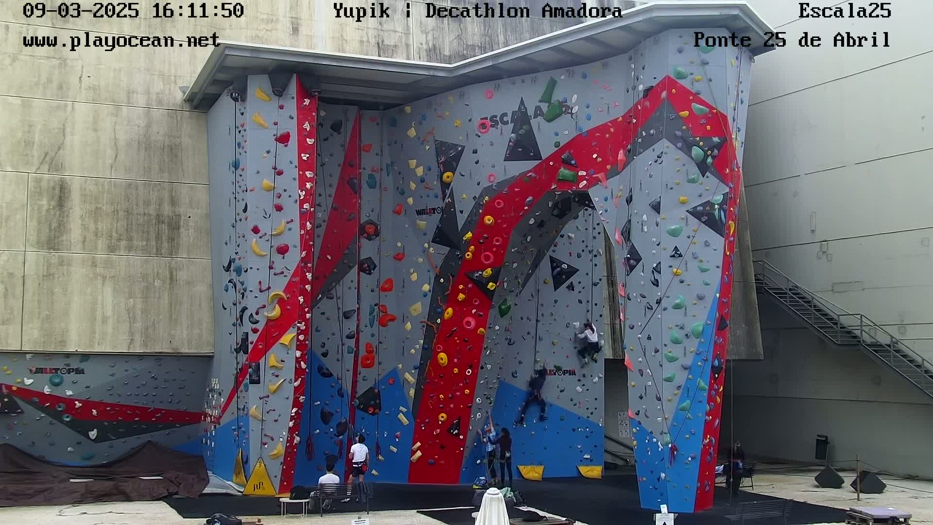 Several people are climbing a large, multicolored outdoor climbing wall.