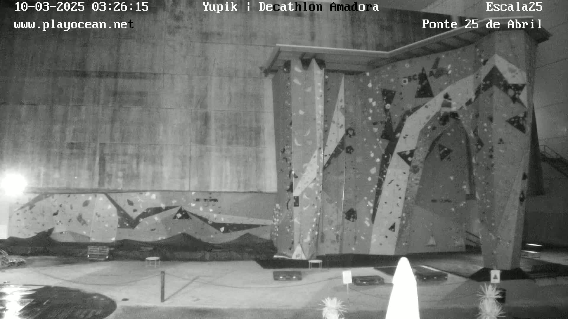 A large indoor climbing wall with various colored holds is illuminated at night.