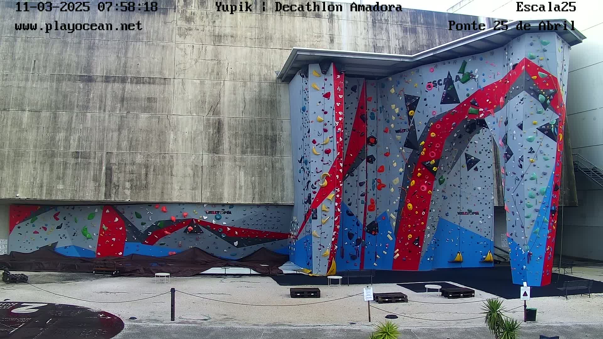 An outdoor view of a large, multi-colored climbing wall attached to a building on an overcast day.