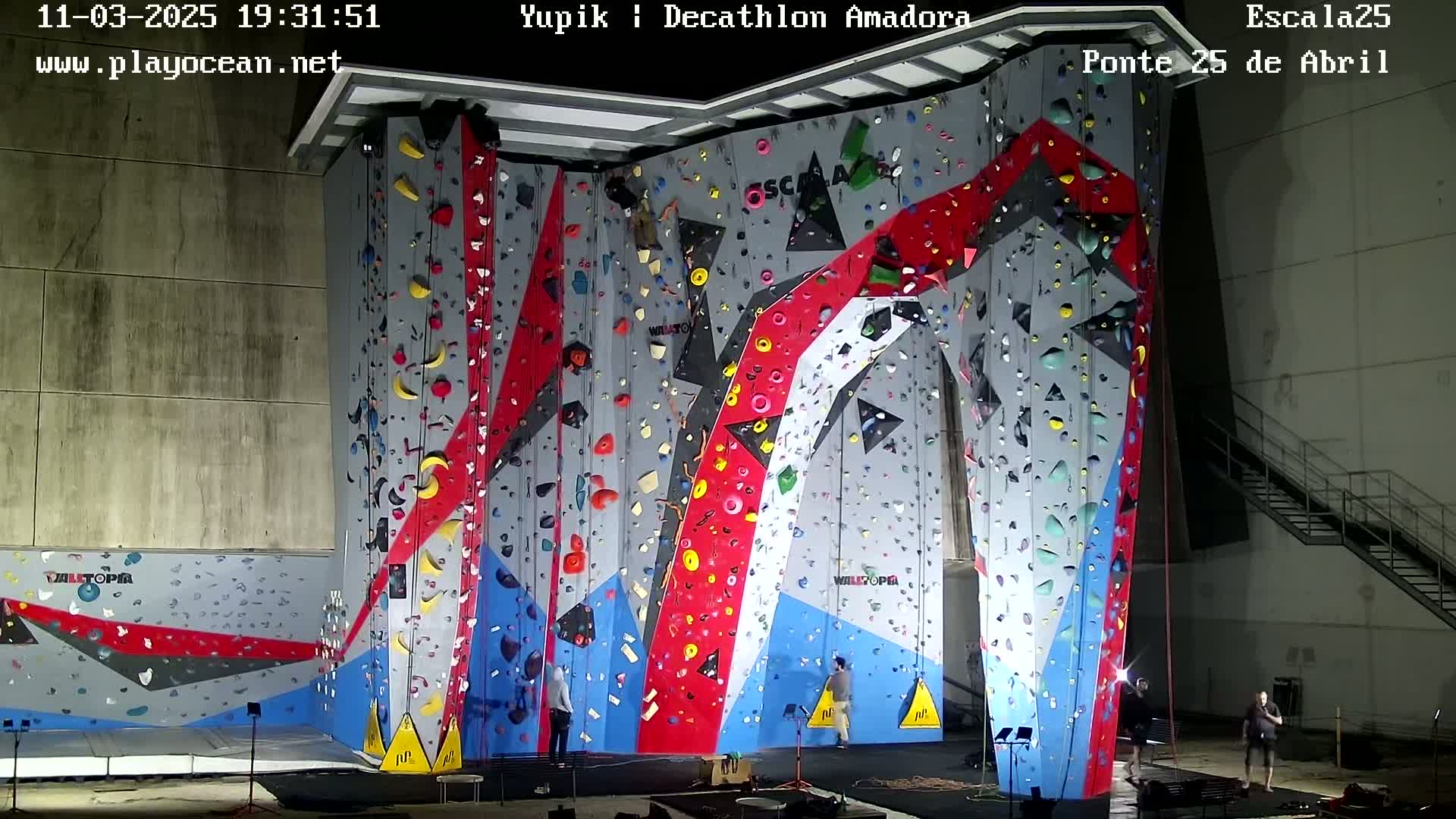 An indoor climbing wall with various colored holds and several people near the base.