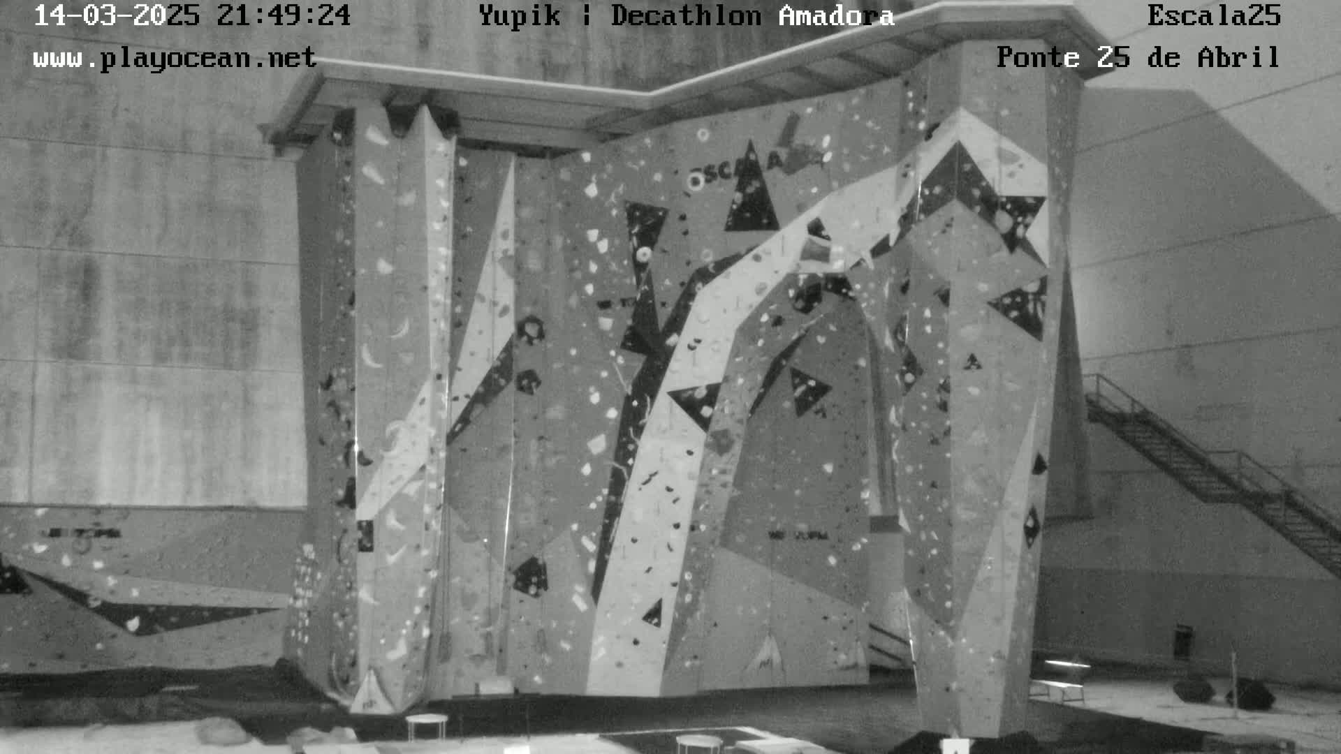 A grayscale image shows an indoor climbing wall with various holds and geometric patterns.