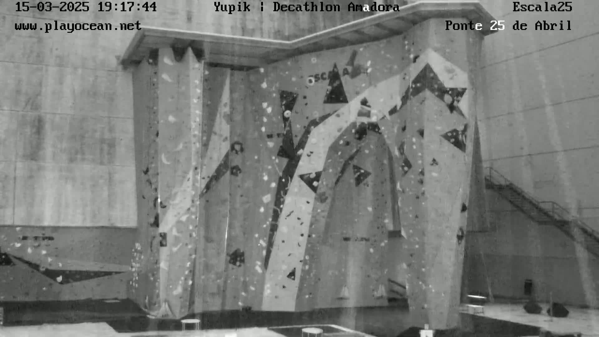 A large indoor climbing wall dominates a monochrome image of a gym-like setting.