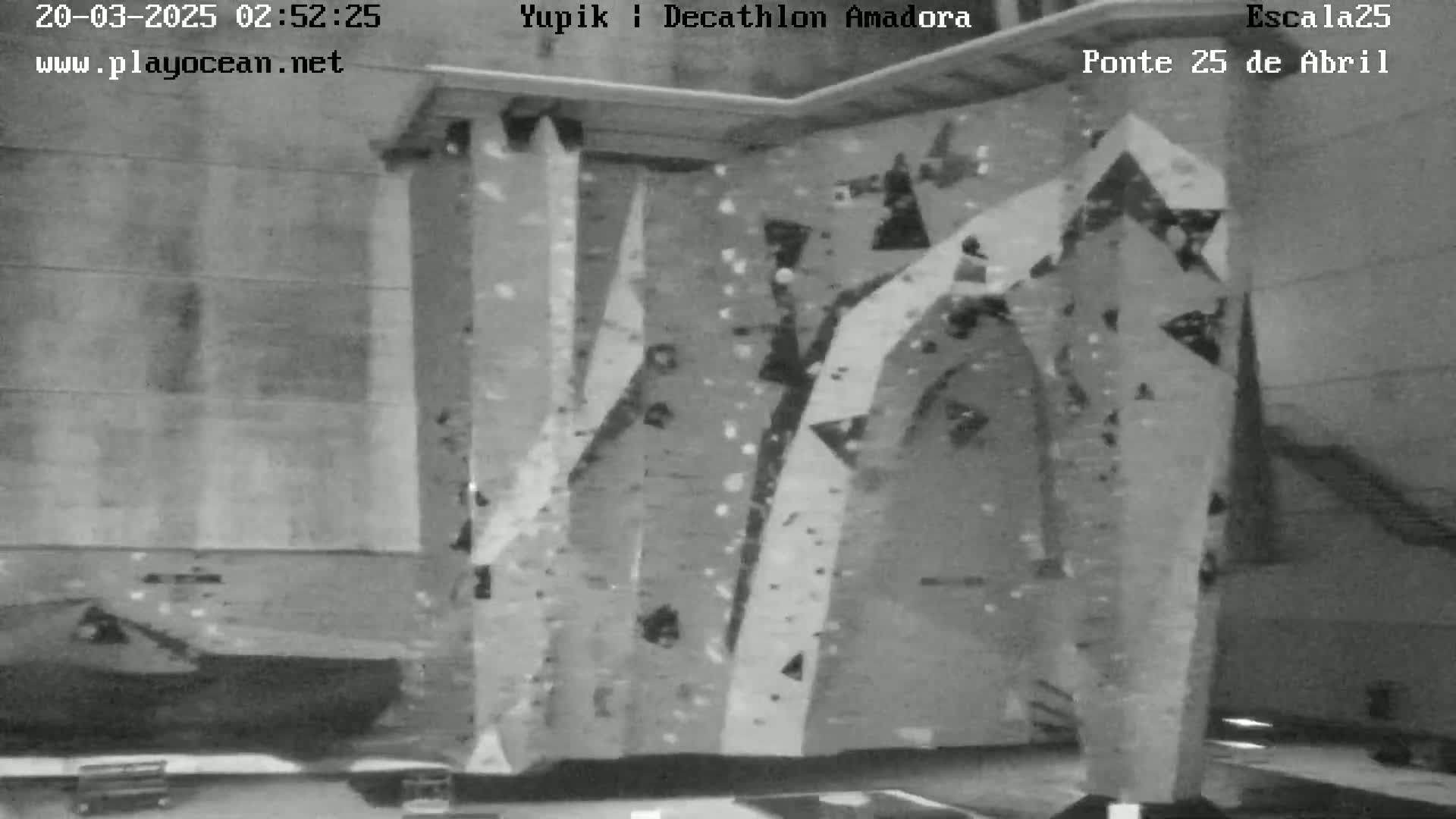 A grayscale image shows an indoor climbing wall with various holds and routes.