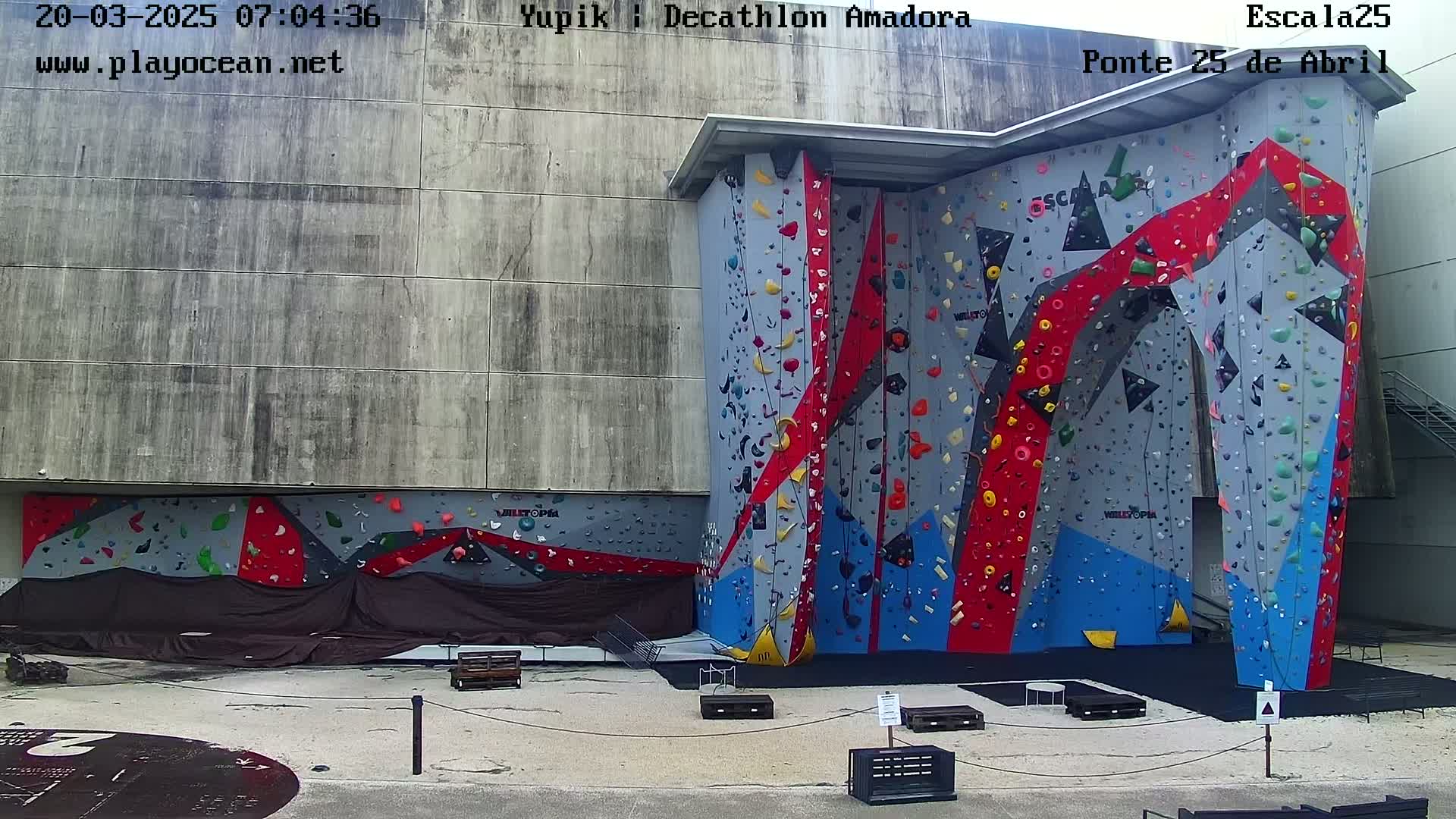 An outdoor, brightly colored climbing wall stands against a gray building on a mostly sunny day.