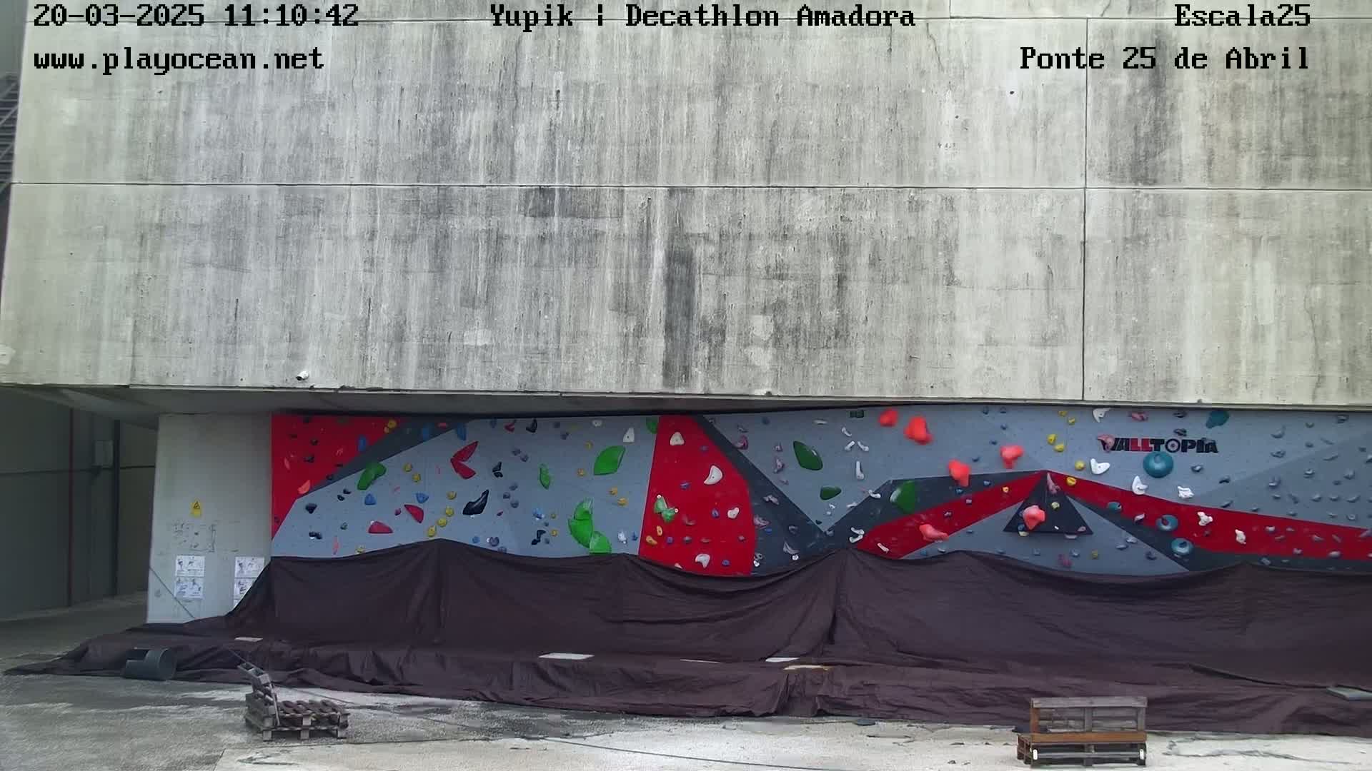 A partially covered outdoor climbing wall is situated against a concrete building under a seemingly overcast sky.